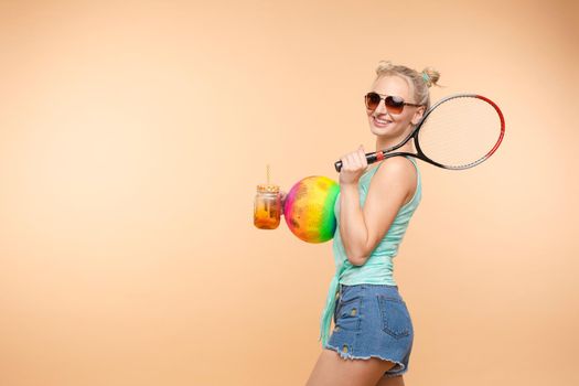 A beautiful woman in a bright outfit, denim shorts with a racket in her hands in the studio. Summer.