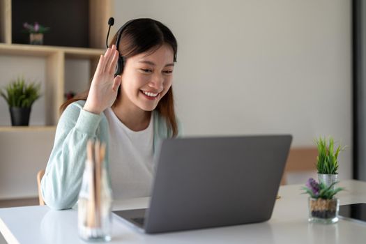 Attractive happy young student studying online at home, using laptop computer, headphones, having video chat, waving. Remote work, distance education. Video conference or virtual event on quarantine.