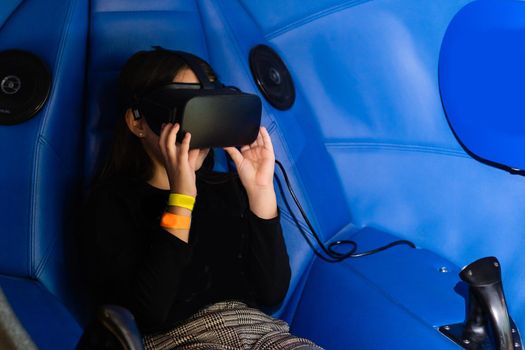 A little girl sitting in a gaming cockpit and holding the race steering wheel to play a racing simulation.