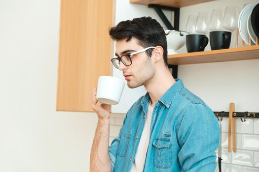 Serious young man drinking tea or coffee in the kitchen, worrying about the situation in the world