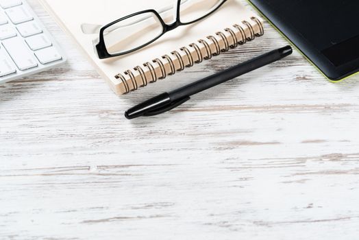 Still life of modern office workspace with copy space. Flat lay composition with computer keyboard and spiral notepad on wooden surface. Time management and day planning. Corporate business workplace