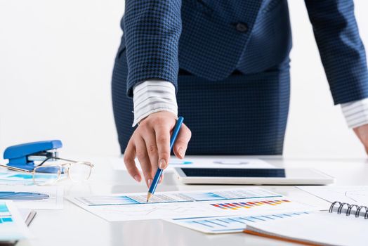 Businesswoman standing near office desk and analyzing financial charts. Successful corporate manager in business suit. Close-up woman hand with pen. Entrepreneurship and leadership concept.