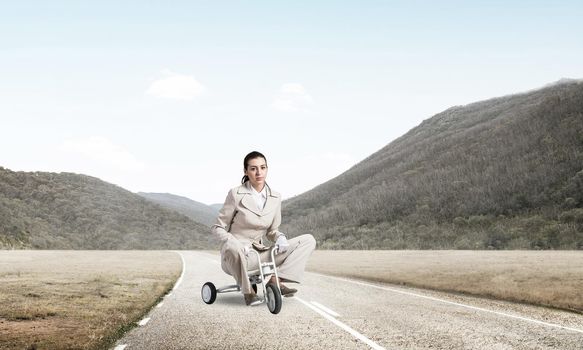 Caucasian woman riding kid's bicycle on asphalt road. Young employee in white business suit biking outdoor. metaphor of ineffective and incompetent work. Beginner level concept with bicyclist.