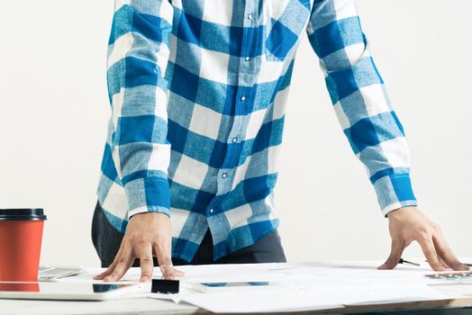 Architect standing near desk with blueprints and cup of coffee. Architecture studio concept with design project. Close up man hand lying on technical drawing. Professional building and engineering.