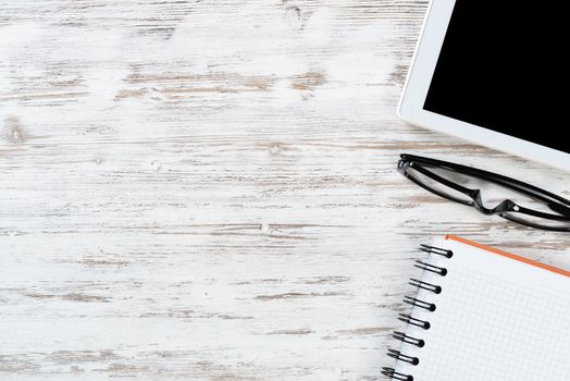 Still life of modern office workspace with copy space. Tablet computer, spiral notebook and glasses on white wooden surface. Time management and day planning. Education, freelance and business concept