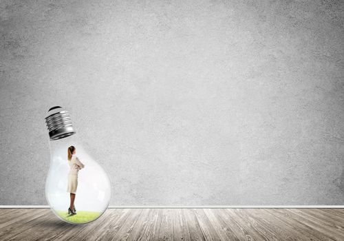 Businesswoman inside of light bulb in empty concrete room