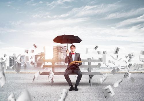 young businessman with umbrella and book, around fly in chaos documents