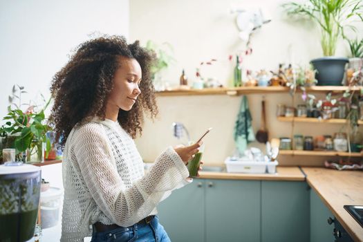 Beautiful young girl browsing on social media while enjoying her green smoothie