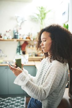 Young african girl browsing on social media while enjoying her green smoothie