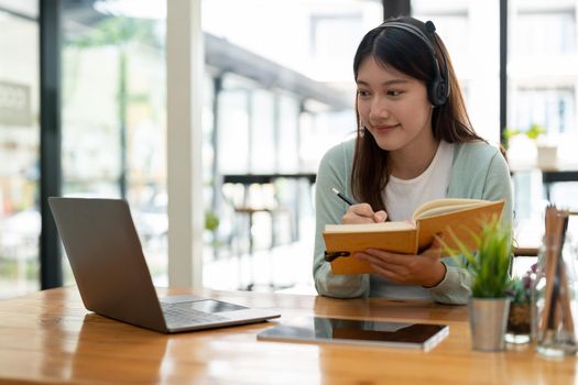 Asian woman writing making list taking notes in notepad working or learning on laptop indoors- educational course or training, seminar, education online concept.