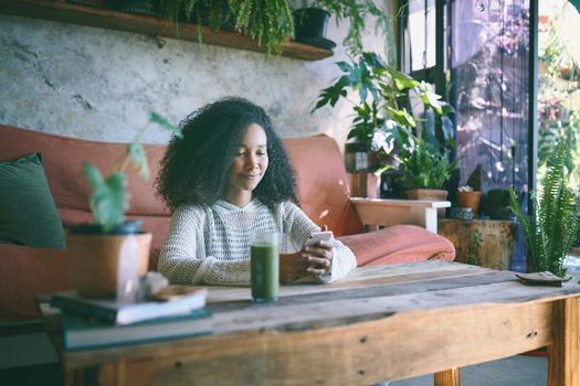 Beautiful girl browsing on social media while enjoying her green smoothie in her lounge