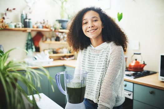 Shot of a young woman smiling at camera while making a healthy smoothie at home