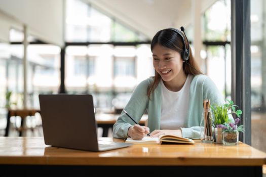 Young asian woman writing making list taking notes in notepad working or learning on laptop indoors- educational course or training, seminar, education online concept.