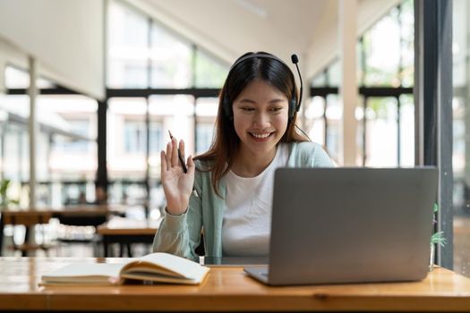 Attractive happy young student studying online at home, using laptop computer, headphones, having video chat, waving. Remote work, distance education. Video conference or virtual event on quarantine.
