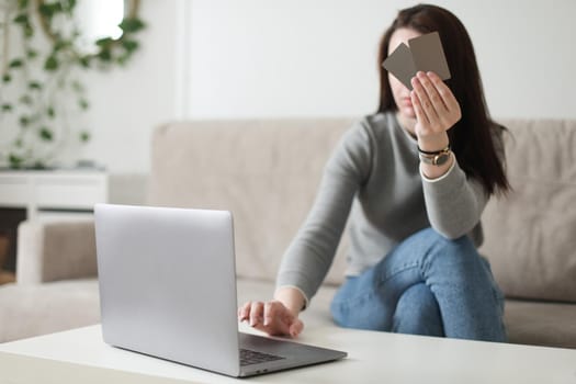Young woman holding credit card and using laptop at home. Paying online, home shopping, internet banking, electronic store concept