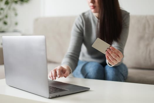 Young woman holding credit card and using laptop at home. Paying online, home shopping, internet banking, electronic store concept.