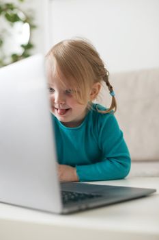 little girl uses a laptop video chat to communicate learning at home, child studying online
