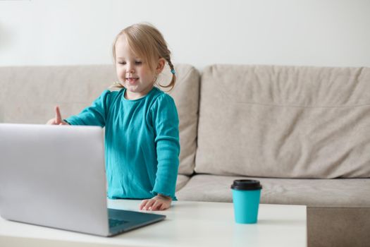 little girl uses a laptop video chat to communicate learning at home, child studying online