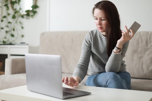 Young woman holding credit card and using laptop at home. Paying online, home shopping, internet banking, electronic store concept.