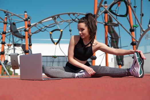 sporty girl does fitness on a sports field in the summer outdoors with a laptop