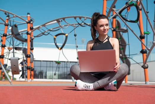 girl in sportswear on a summer outdoor sports field is sitting with a laptop
