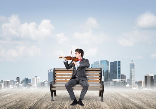 Young businessman plays the violin sitting on a wooden bench. Inspiration in business