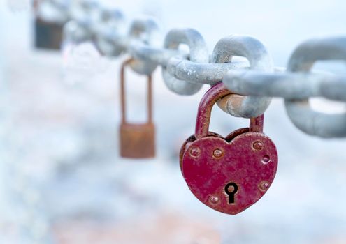 A red heart-shaped lock hangs from the bridge chain. The wedding custom is a symbol of eternal love. Close-up.