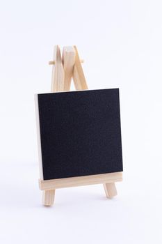Wooden Easel Miniature with Blank Black Square Canvas for Artists and Painters - Mockup. Mini Wooden Stand with Clean Artboard on White Background, Copy Space