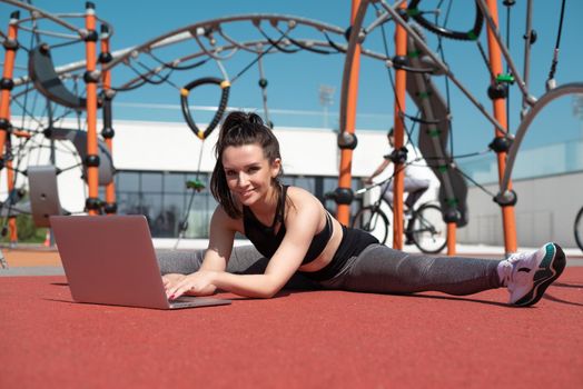 sporty girl does fitness on a sports field in the summer outdoors with a laptop