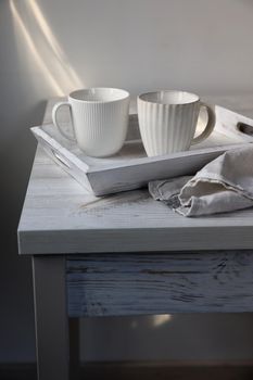 Two corrugated mugs on a white tray and a kitchen towel on a beige table against a white wall. Scandinavian style. Minimalism. Place for text