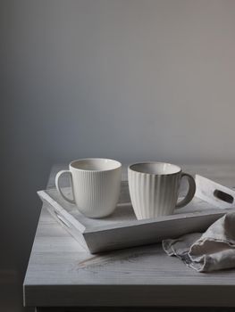 Two corrugated mugs on a white tray and a kitchen towel on a beige table against a white wall. Scandinavian style. Minimalism. Place for text