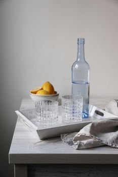 A blue transparent water bottle and two ribbed glasses on a white wooden tray on the kitchen table.