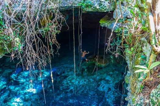 Traveler and tourist guide at amazing blue turquoise water and limestone cave sinkhole cenote Tajma ha Tajmaha in Puerto Aventuras Quintana Roo Mexico.