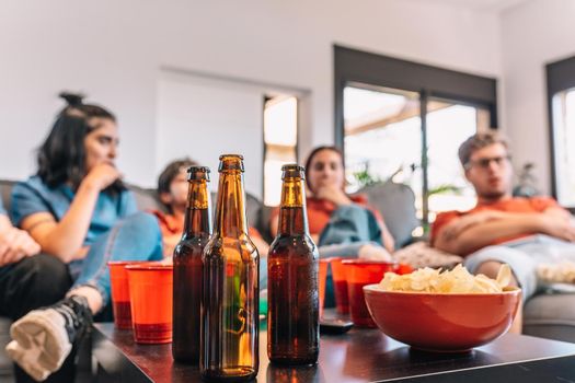 Close-up of a table full of drinks and snacks for a party. Friends watching football in the living room. concept of leisure. concept of friendship. group of six people, friendly relationship, divided teams, red and blue, competitive.