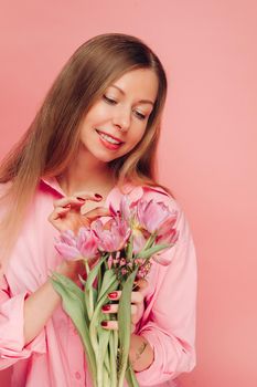 A sweet charming woman with flowers in a pink dress on a pink background smiles, happiness and luck.