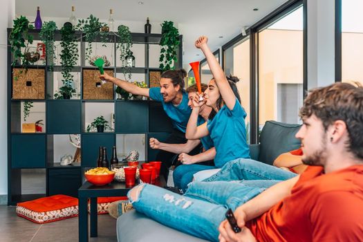 young friends competing on behalf of their sports team. friends celebrating victory. friends sad after defeat. watching sport on TV. leisure concept, three young adults in blue t-shirts. happy and cheerful. natural light in the living room at home.