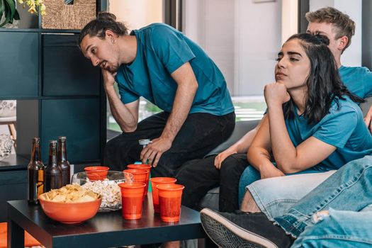 Football fans saddened by their team's defeat. Friends watching football in living room concept of leisure. concept of friendship. group of six people, friendly relationship, divided teams, red and blue, competitive.