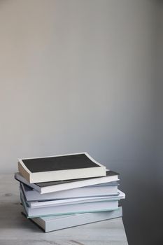 Stack of books on a beige table against a white wall. Scandinavian style. Minimalism. Place for text