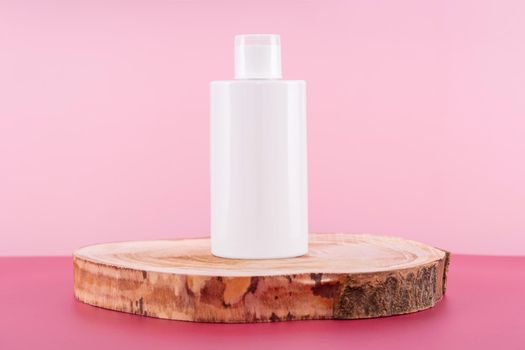 Cleaning agent, softener or liquid soap bottle on round wooden podium. Presentation of detergent mockup on pink background. Home sanitary liquid for laundry in plastic container mock up