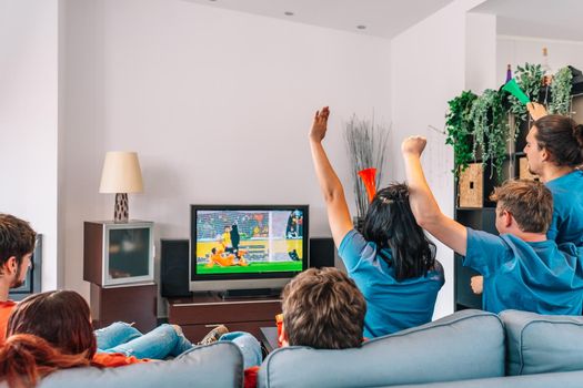 young friends competing on behalf of their sports team. friends celebrating victory. friends sad after defeat. watching sport on TV. leisure concept, three young adults in blue t-shirts. happy and cheerful. natural light in the living room at home.