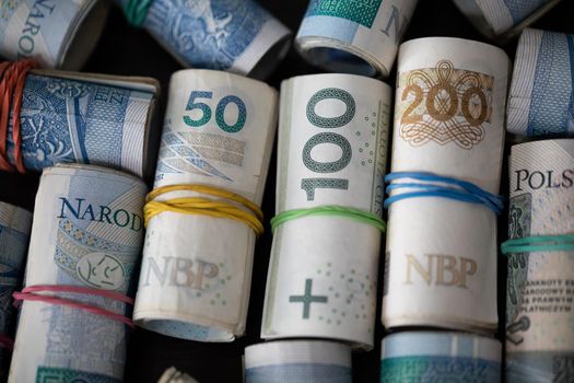 Several rolls of Polish banknotes in top view. Rolled up and fastened with a thin rubber band.