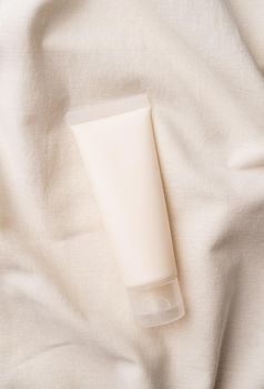 Mockup facial skincare product white tube with blank label on farbic wavy background, Top view