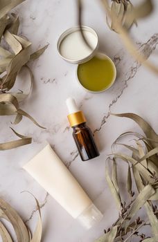 Natural cosmetics. Essential oil bottle, cream tube mockup, plastic bottle with cosmetic product on marble and eucalyptus leaves