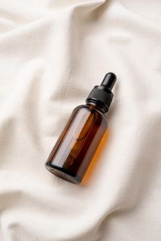 top view of amber glass essential oil droppper bottle with pipette on fabric wavy background, mockup design