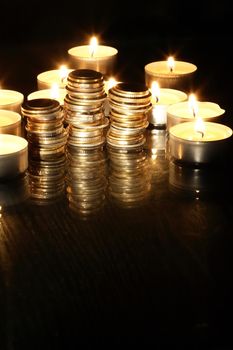 Set of coins between lighting candles on dark background