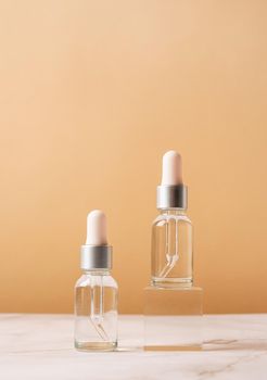 Glass dropper bottles with a pippette with black rubber tip on glass podium and beige background. Nature Skin concept. Organic Spa Cosmetics. Trendy concept.