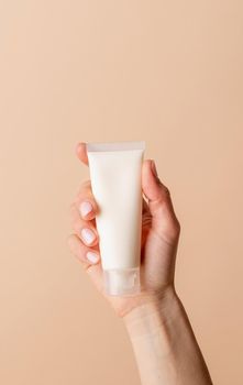 Natural cosmetics. Face cream Mock-Up. Female hand holding white cream tube on beige background