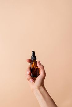 Natural cosmetics. Dropper Bottle Mock-Up. Female hand holding amber glass dropper bottle on beige background