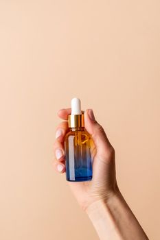 Natural cosmetics. Dropper Bottle Mock-Up. Female hand holding amber glass dropper bottle on beige background