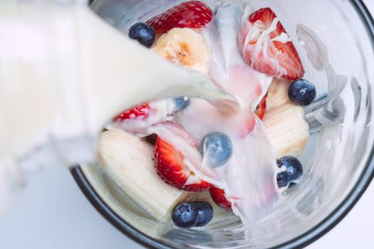 Making smoothie or milkshake in blender. Pouring milk in a blender with fruits. Vegan smoothie with almond milk. High quality photo